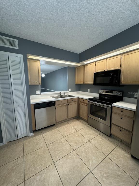 A kitchen features light wood cabinets, stainless steel appliances, and beige tile flooring — 13815 TIMBERLAND DRIVE UNIT 103, ORLANDO, FL