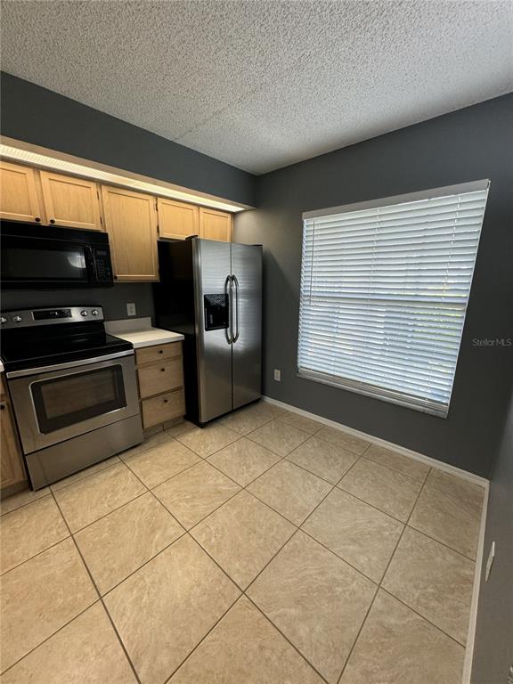 A kitchen features light wood cabinets, stainless steel appliances, and beige tile flooring — 13815 TIMBERLAND DRIVE UNIT 103, ORLANDO, FL