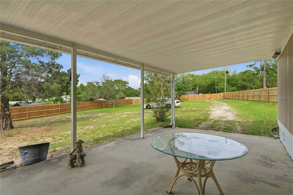 A covered concrete patio features a glass-topped table and overlooks a fenced backyard — 5494 S OLDFIELD AVENUE, HOMOSASSA, FL