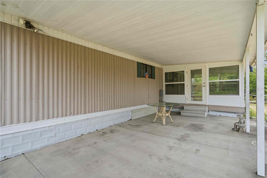 A covered concrete patio features tan metal siding, a glass table, and a glass door — 5494 S OLDFIELD AVENUE, HOMOSASSA, FL