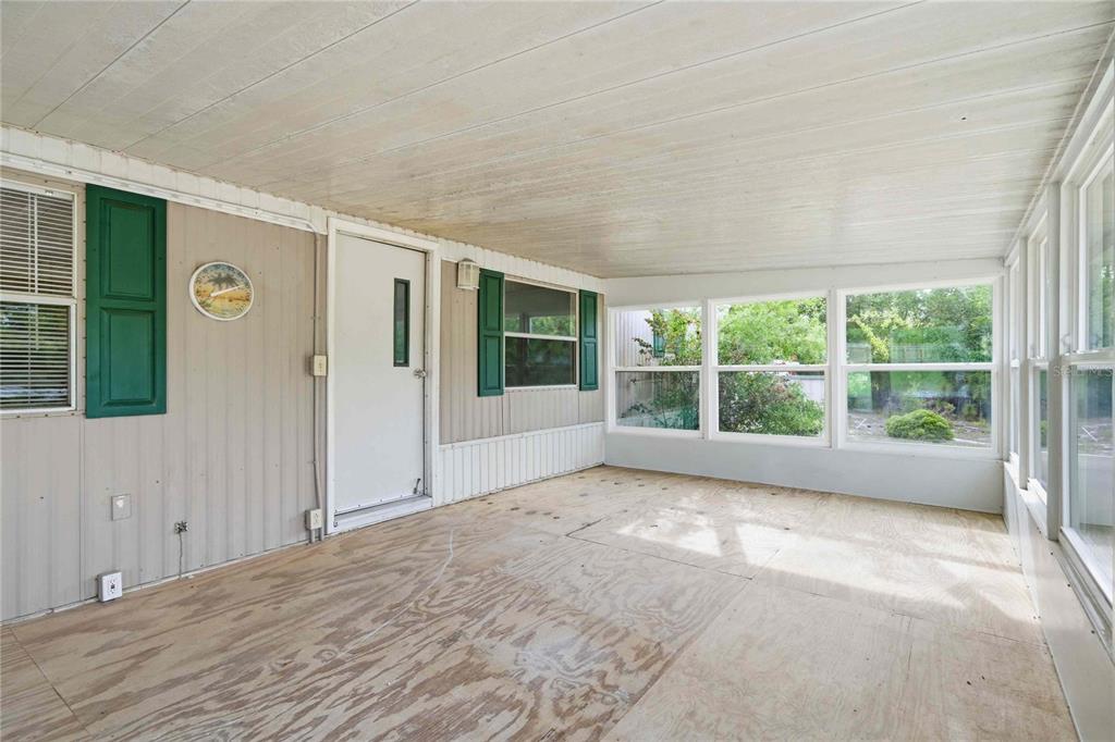 An enclosed porch features plywood flooring, white paneled walls, and multiple windows with green shutters — 5494 S OLDFIELD AVENUE, HOMOSASSA, FL