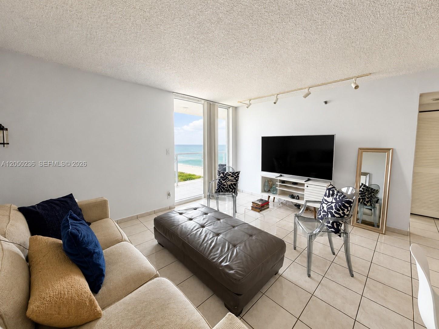 A living room features a beige sofa, leather ottoman, and a balcony with ocean views — 2401 Collins Ave # 1612, Miami Beach FL 33140, MIAMI BEACH, FL
