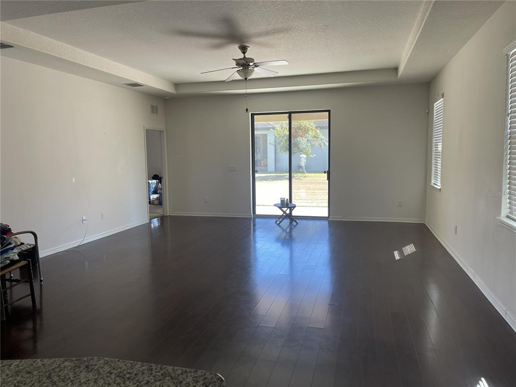A spacious living room features dark hardwood floors, a tray ceiling, and sliding glass doors — 12433 BALLENTRAE FOREST DRIVE, RIVERVIEW, FL