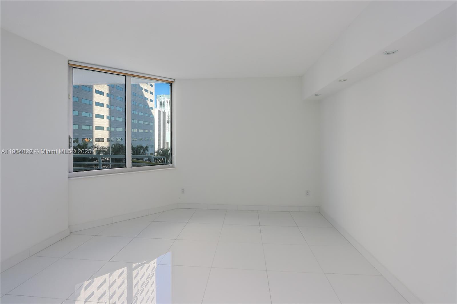 An empty room with white walls, white tile flooring, and a large window overlooking buildings — 325 S Biscayne Blvd # 1722, Miami FL 33131, MIAMI, FL