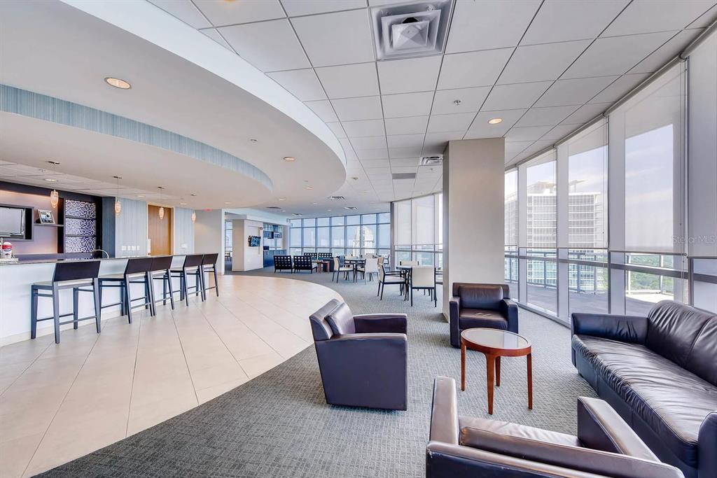 A modern lounge area features a bar, seating groups, and floor-to-ceiling windows with city views — 111-3 WASHINGTON STREET, ORLANDO, FL