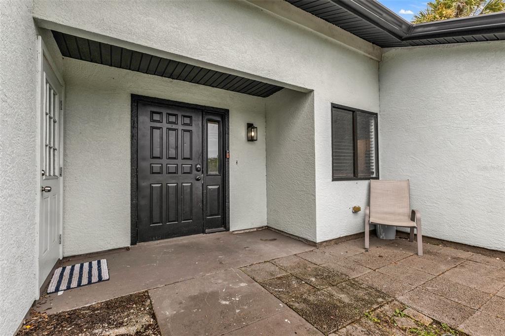 A covered entryway features a black front door, a side door, and a patio chair — 975 BAER AVENUE NW, PORT CHARLOTTE, FL