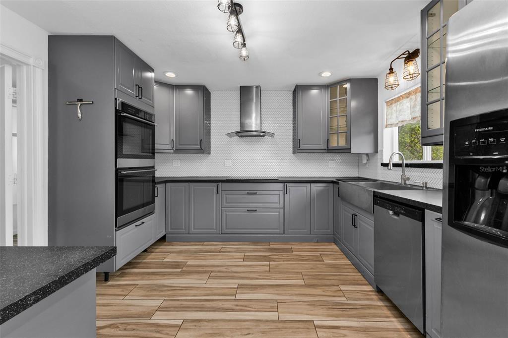A kitchen features gray cabinets, stainless steel appliances, a herringbone backsplash, and wood-look tile flooring — 975 BAER AVENUE NW, PORT CHARLOTTE, FL