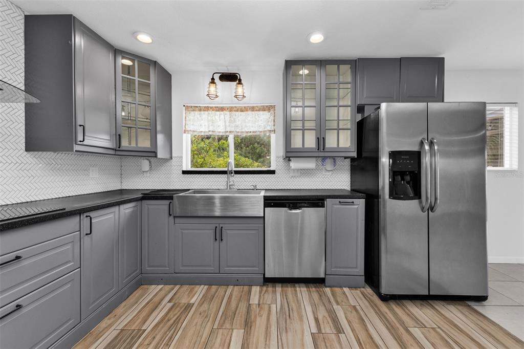 A kitchen features gray cabinets, stainless steel appliances, a farmhouse sink, and wood-look tile flooring — 975 BAER AVENUE NW, PORT CHARLOTTE, FL