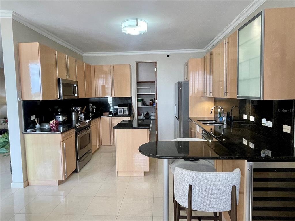 A kitchen features light wood cabinets, black countertops, stainless steel appliances, and a breakfast bar — Palma Real Avenue MURANO LUXURY APARTMENTS UNIT 8, GUAYNABO, PR