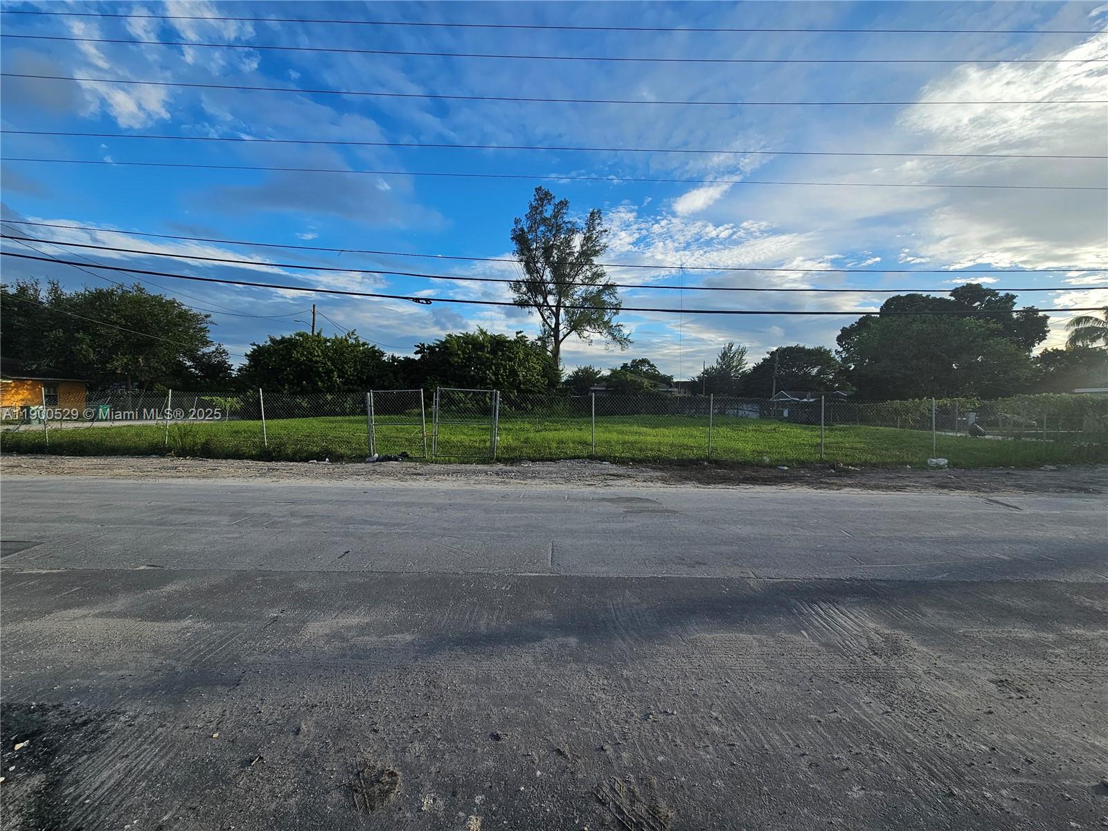A fenced, grassy vacant lot sits along a paved road under a blue sky — 2140 NW 76th St, Miami FL 33147, MIAMI, FL