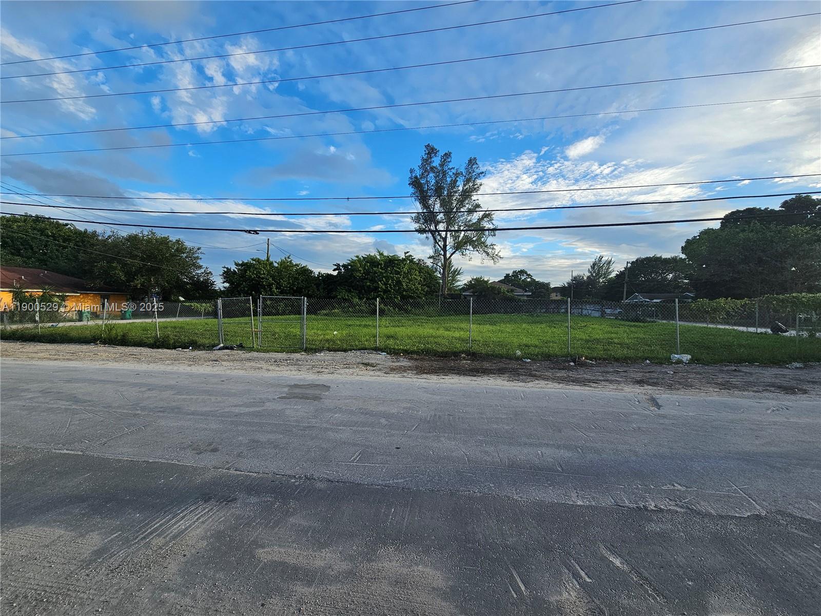 A fenced, grassy vacant lot sits along a paved road under a cloudy sky — 2140 NW 76th St, Miami FL 33147, MIAMI, FL