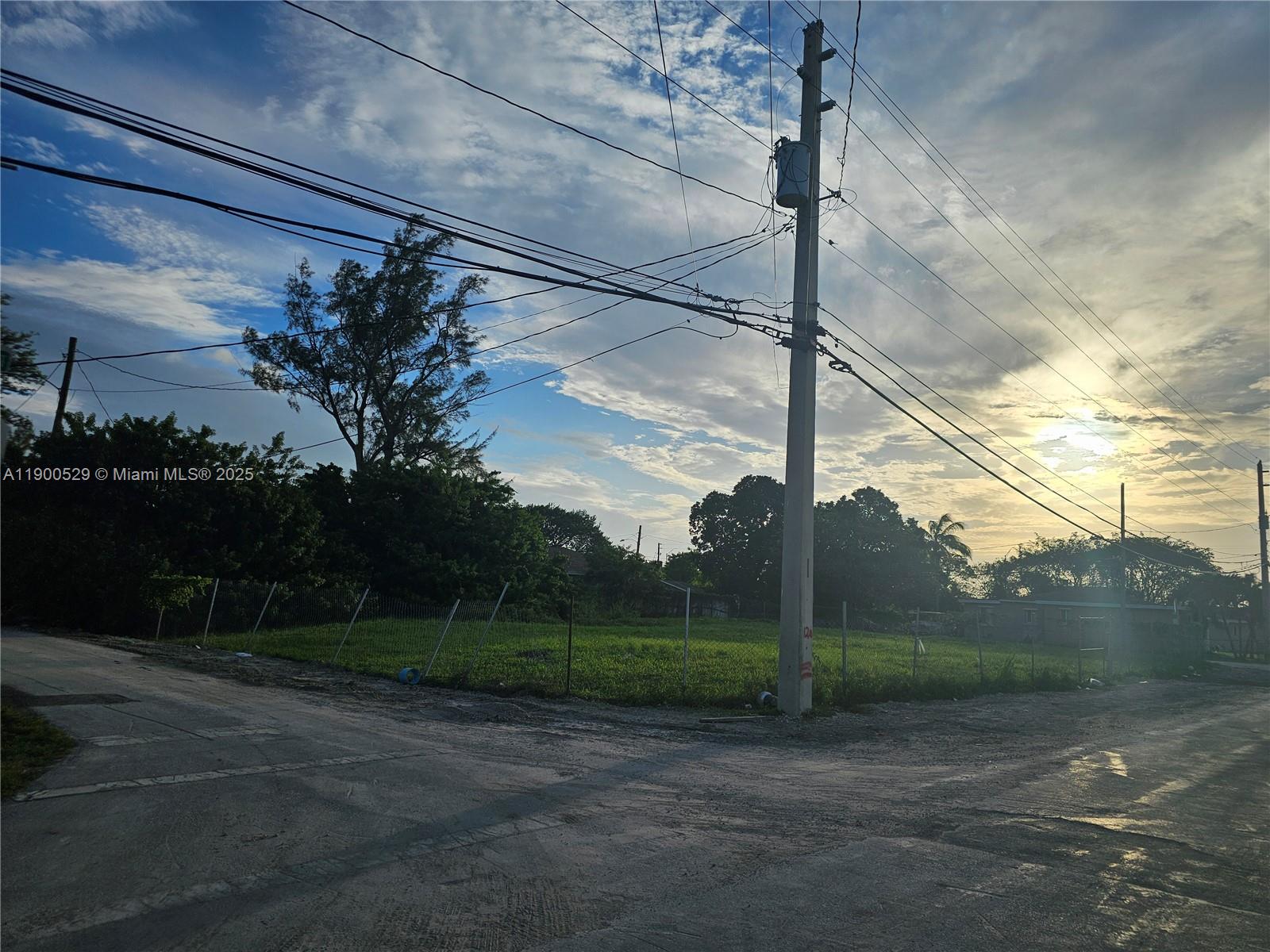 A vacant, fenced grassy lot sits at a street corner under a cloudy sky — 2140 NW 76th St, Miami FL 33147, MIAMI, FL