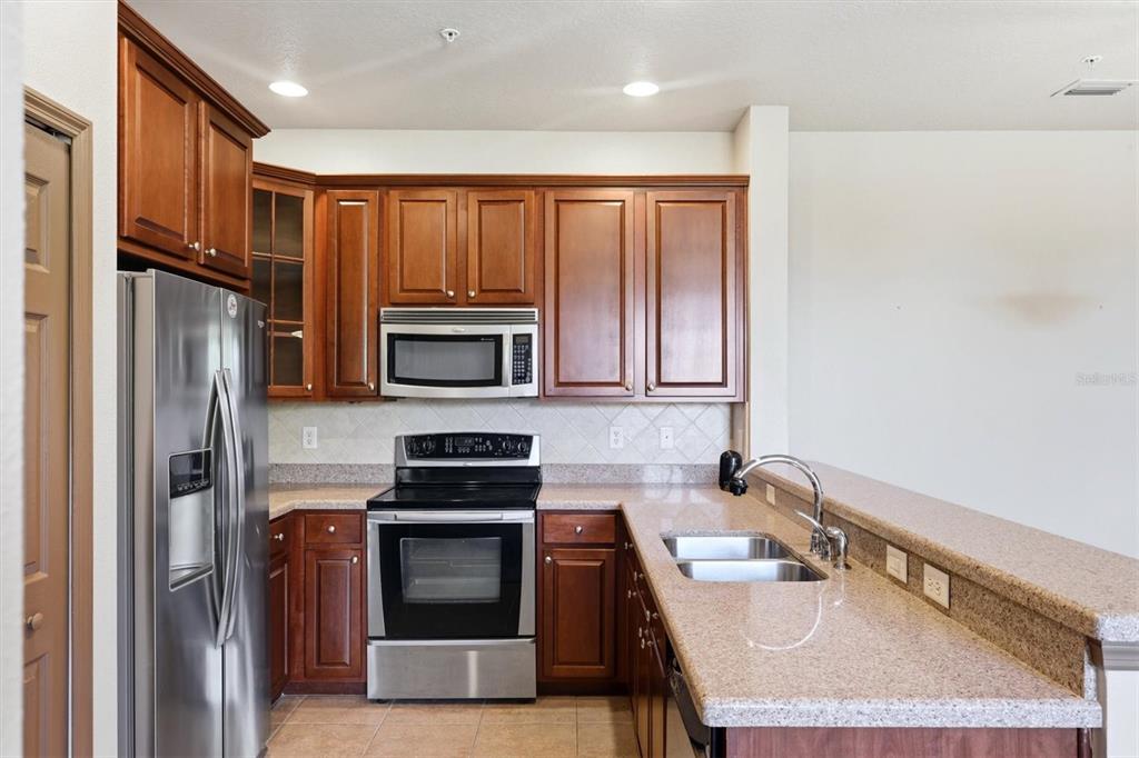 A kitchen features wood cabinets, stainless steel appliances, and granite countertops with a breakfast bar — 8098 MOONSTONE DRIVE UNIT 17-203, SARASOTA, FL