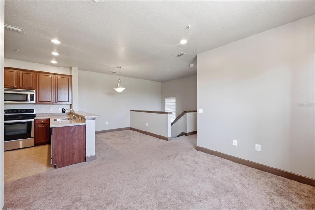 An open-concept kitchen with wood cabinets and a carpeted living area overlooking a staircase — 8098 MOONSTONE DRIVE UNIT 17-203, SARASOTA, FL