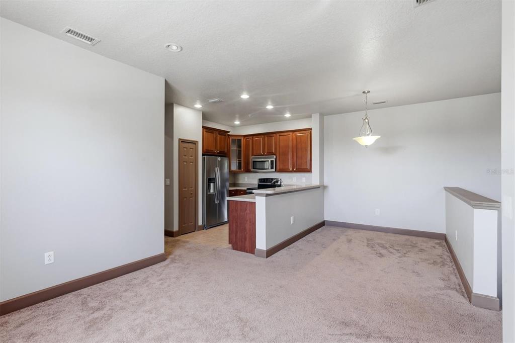 A kitchen with wood cabinets and stainless steel appliances overlooks a carpeted dining area — 8098 MOONSTONE DRIVE UNIT 17-203, SARASOTA, FL