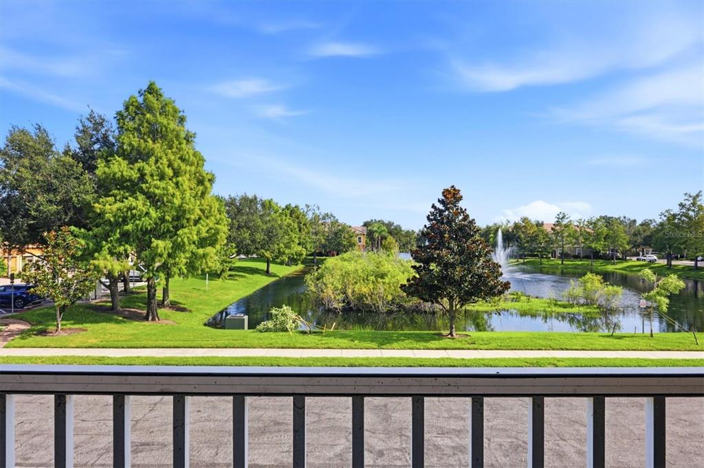 A balcony view overlooks a grassy lawn, a pond with a fountain, and surrounding trees — 8098 MOONSTONE DRIVE UNIT 17-203, SARASOTA, FL