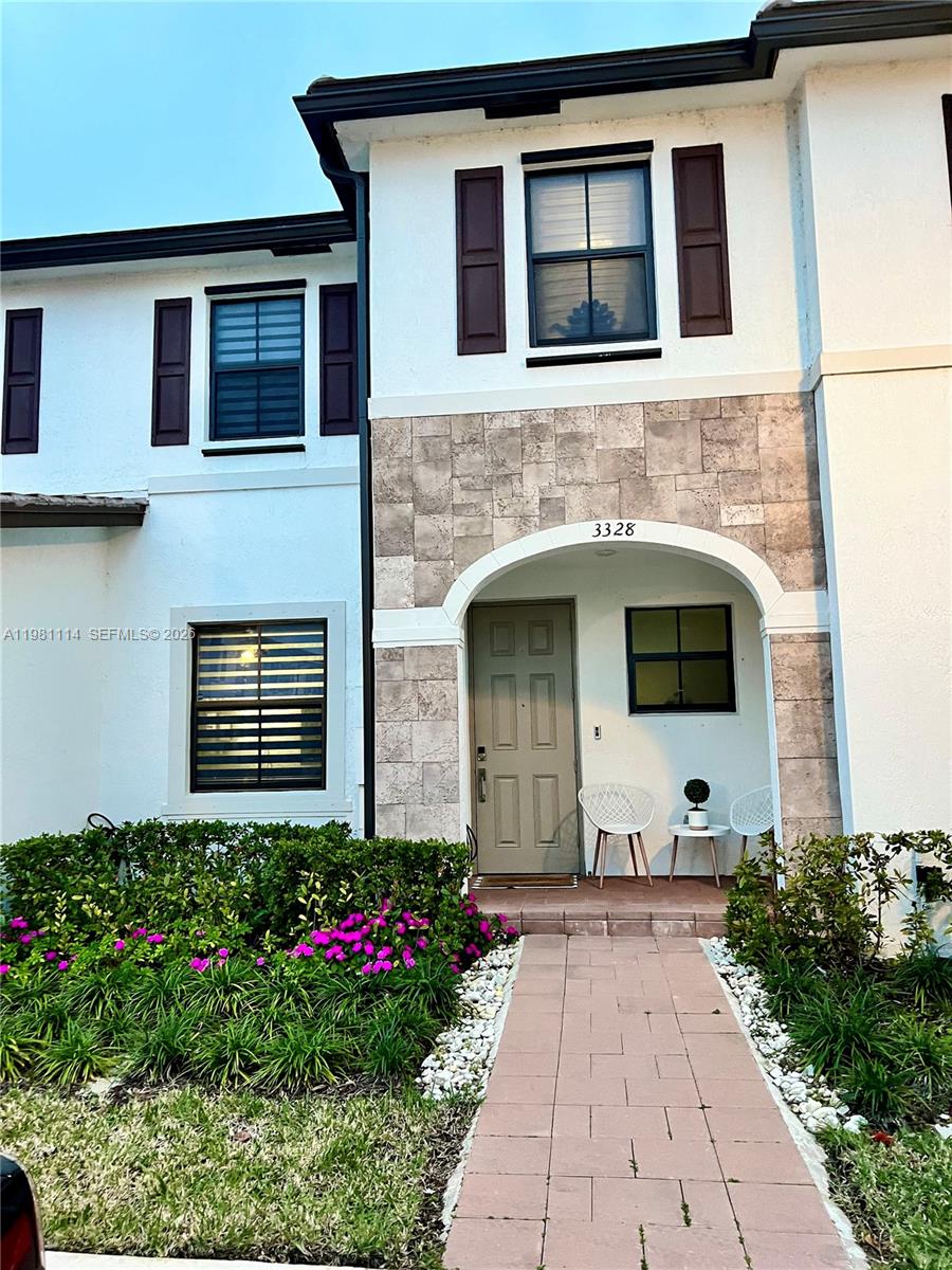 A two-story townhouse exterior features a stone-accented entryway, a paved walkway, and purple flowers — 3328 W 114th Ter # 3328, Hialeah FL 33018, HIALEAH, FL
