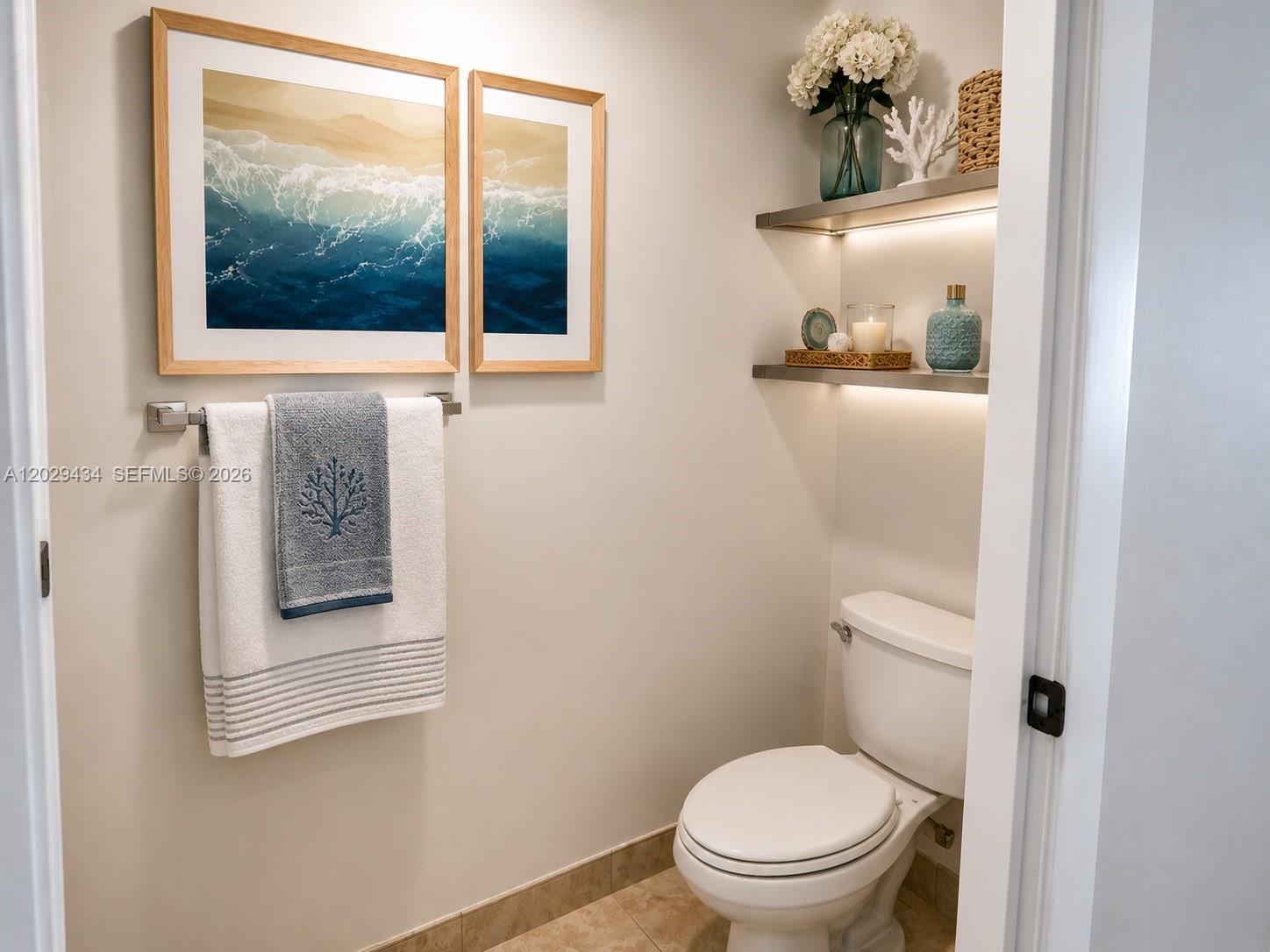 A small bathroom features a toilet, floating shelves with decor, and coastal-themed wall art — 90 SW 3rd St # 1703, Miami FL 33130, MIAMI, FL