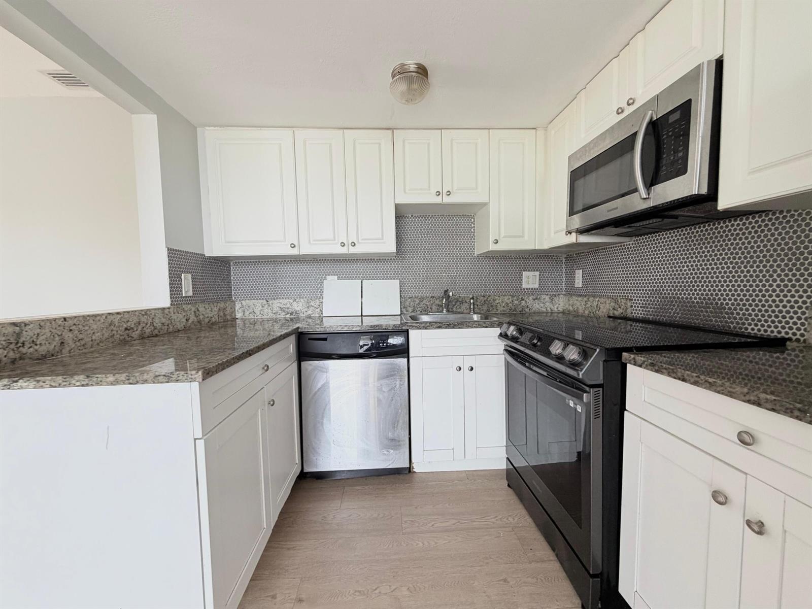 A kitchen features white cabinets, granite countertops, a stainless steel dishwasher, and a black stove — 1501 Crescent Circle # E45, Lake Park FL 33403, LAKE PARK, FL