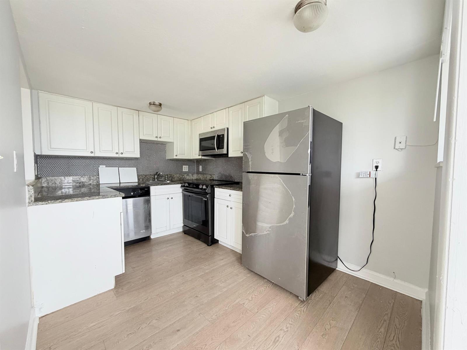 A kitchen features white cabinets, granite countertops, stainless steel appliances, and light wood flooring — 1501 Crescent Circle # E45, Lake Park FL 33403, LAKE PARK, FL
