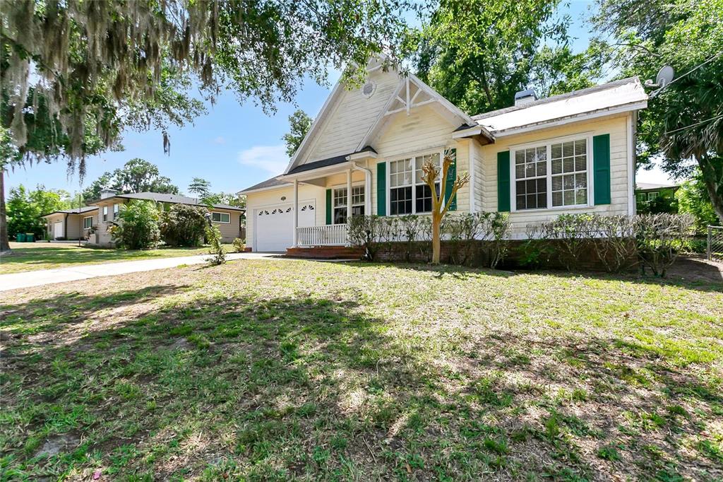 A yellow single-story house with a white garage and green shutters sits on a lawn — 1311 HILLTOP DRIVE, MOUNT DORA, FL