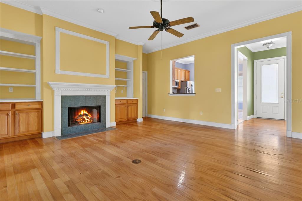 A living room with yellow walls, hardwood floors, a fireplace, and built-in shelving — 1311 HILLTOP DRIVE, MOUNT DORA, FL