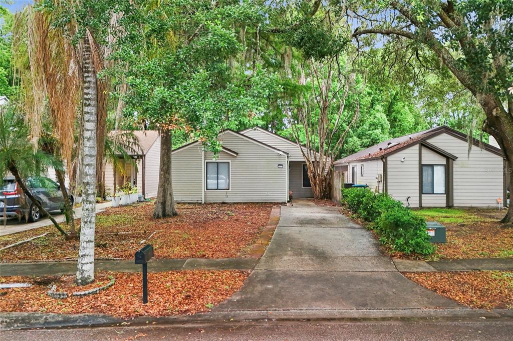 A single-story house with light gray siding and a concrete driveway sits under large trees — 335 KIRKCALDY DRIVE, WINTER SPRINGS, FL