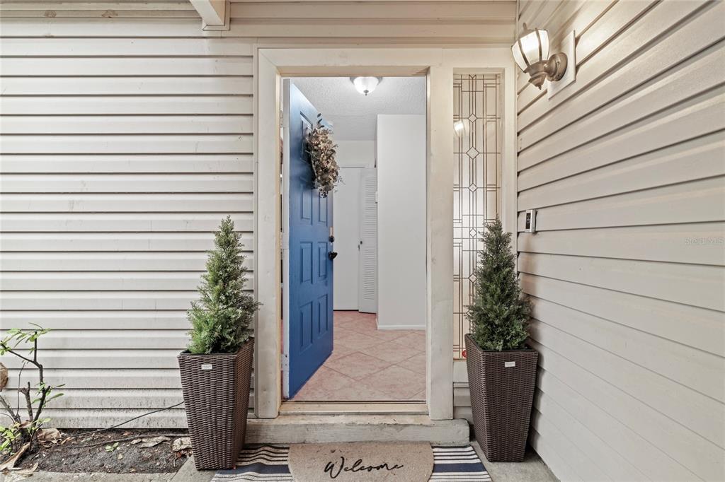 A blue front door opens into a tiled entryway flanked by two potted evergreen trees — 335 KIRKCALDY DRIVE, WINTER SPRINGS, FL