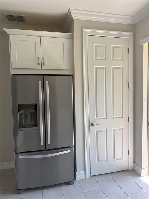 A stainless steel refrigerator sits beneath white cabinets next to a closed interior door — 120 MOSCATA WAY, NOKOMIS, FL