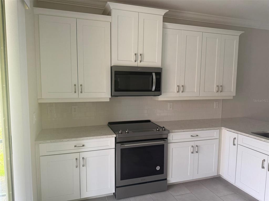 A kitchen features white shaker cabinets, stainless steel appliances, and light-colored quartz countertops — 120 MOSCATA WAY, NOKOMIS, FL