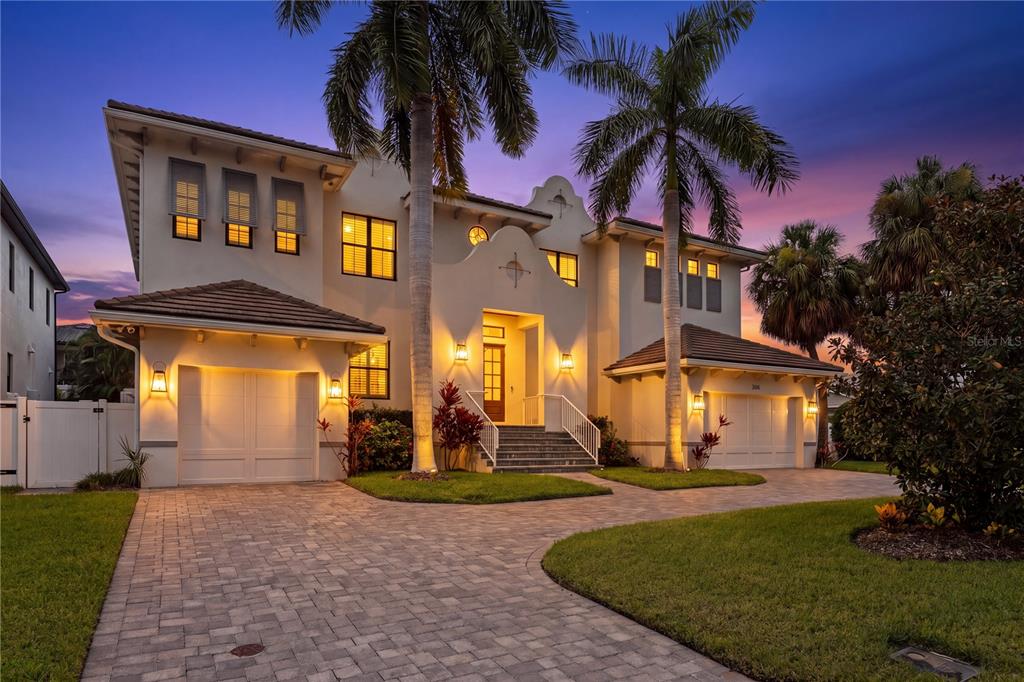 A two-story stucco house with a paved driveway, two garages, and palm trees at dusk — 5015 W LONGFELLOW AVENUE, TAMPA, FL