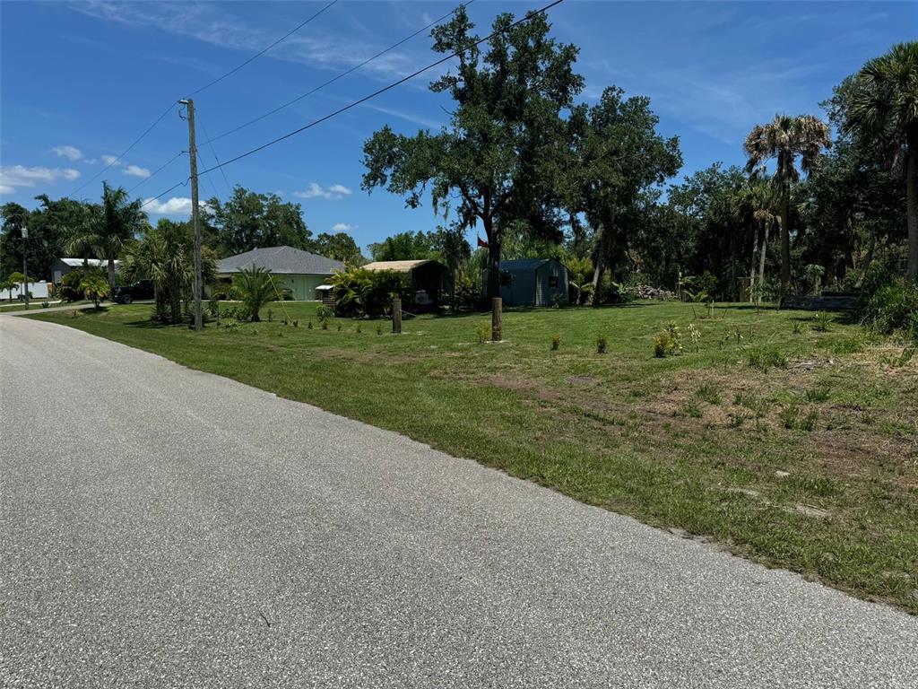 A paved road runs alongside a grassy lot with trees, shrubs, and a small shed — * NAMATKA AVENUE UNIT 21, NORTH PORT, FL