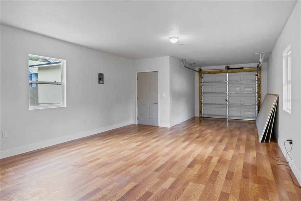 A garage with light wood flooring, a grey door, a window, and a roll-up door — 8514 N MITCHELL AVENUE, TAMPA, FL