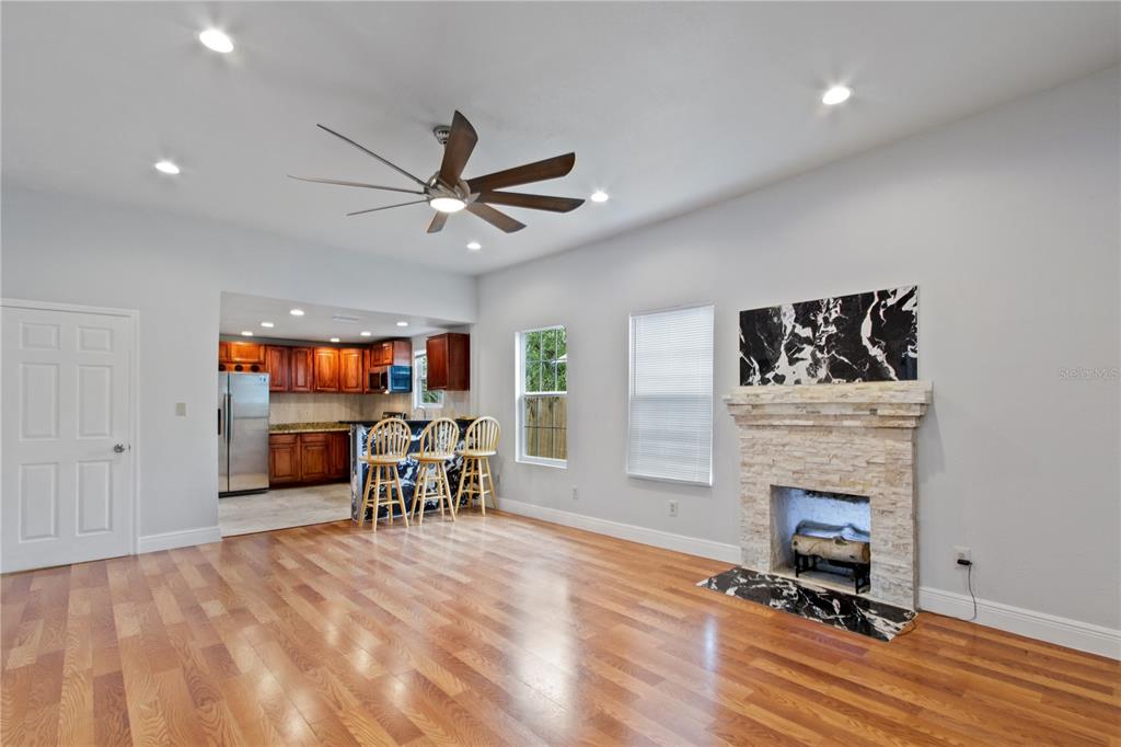 A living room with hardwood floors, a stone fireplace, and an open kitchen with bar seating — 8514 N MITCHELL AVENUE, TAMPA, FL