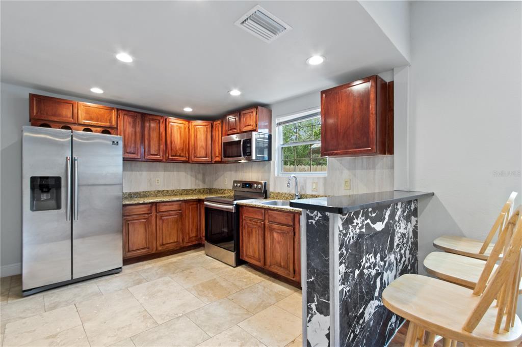 A kitchen with wood cabinets, stainless steel appliances, granite countertops, and a black marble-patterned island — 8514 N MITCHELL AVENUE, TAMPA, FL