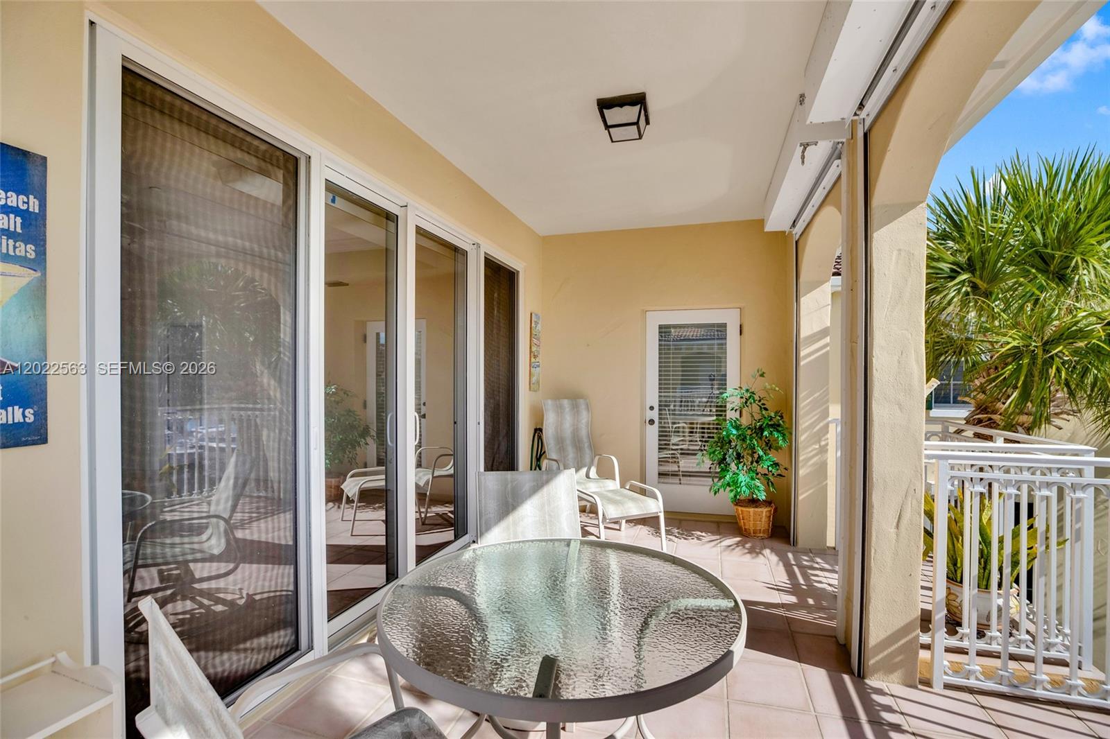 A covered balcony features a glass-topped table, chairs, a potted plant, and sliding glass doors — VERO BEACH, FL