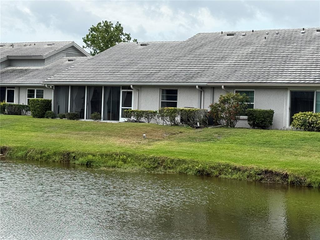 A view of the rear exterior of a single-story house overlooking a small pond — 5371 CRESTLAKE BOULEVARD UNIT 68, SARASOTA, FL