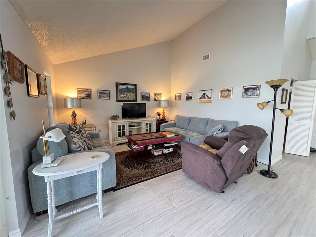 A living room features a blue sofa, a brown recliner, a coffee table, and wall art — 5371 CRESTLAKE BOULEVARD UNIT 68, SARASOTA, FL