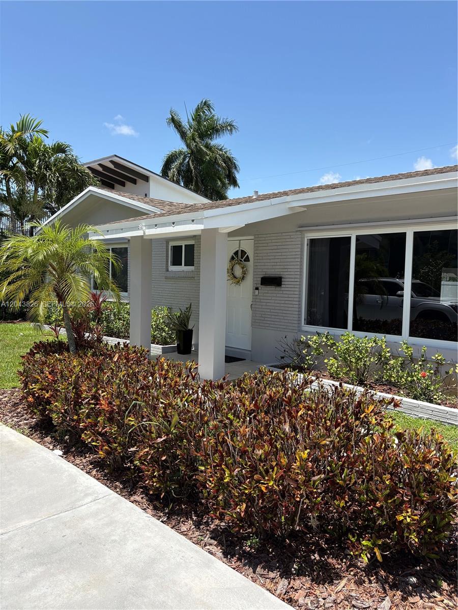 A gray brick house features a white covered porch, a front door with a wreath, and landscaping — 3397 NE 20th Ave, Oakland Park FL 33306, OAKLAND PARK, FL