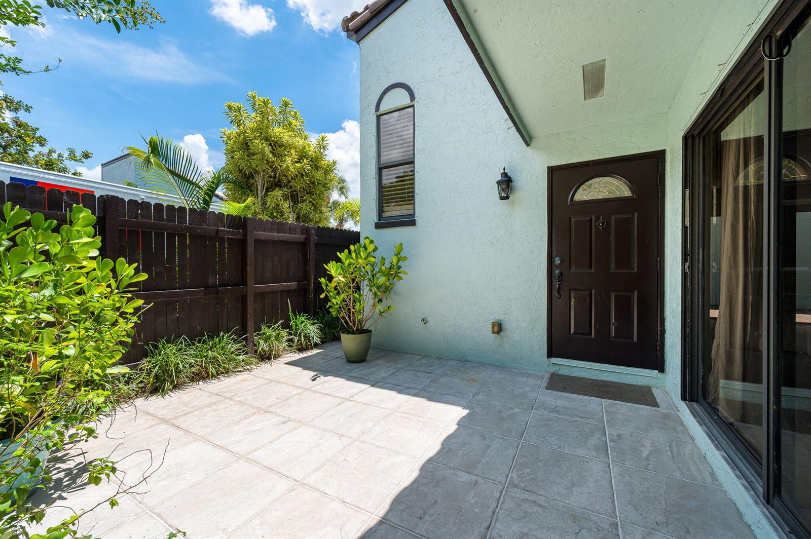 A patio with light-colored tile flooring sits beside a light blue house with a dark door — 22300 Pineapple Walk Drive, Boca Raton FL 33433, BOCA RATON, FL