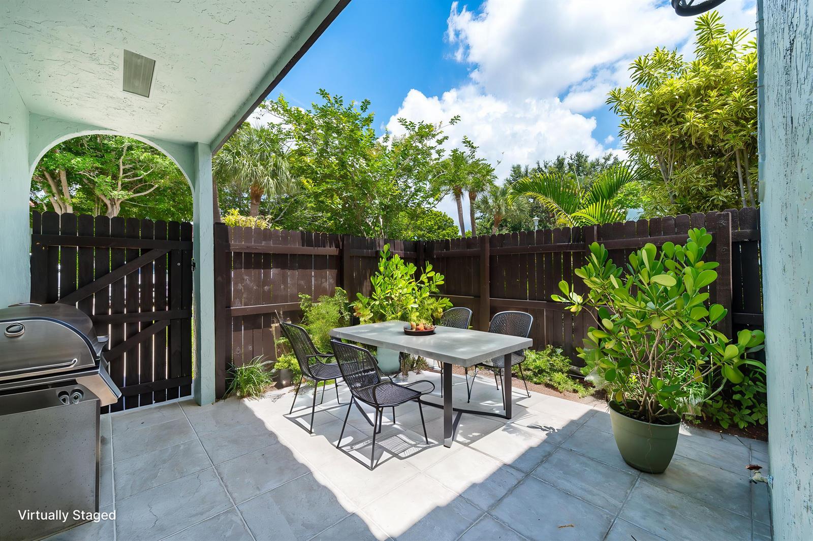 A patio features a dining set, a grill, and potted plants against a wooden fence — 22300 Pineapple Walk Drive, Boca Raton FL 33433, BOCA RATON, FL