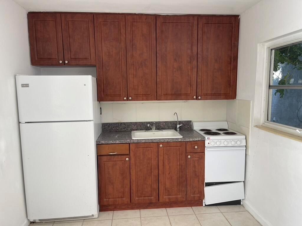A small kitchen features dark wood cabinets, a white refrigerator, a sink, and a stove — 115 E Lantana Road, Lantana FL 33462, LANTANA, FL