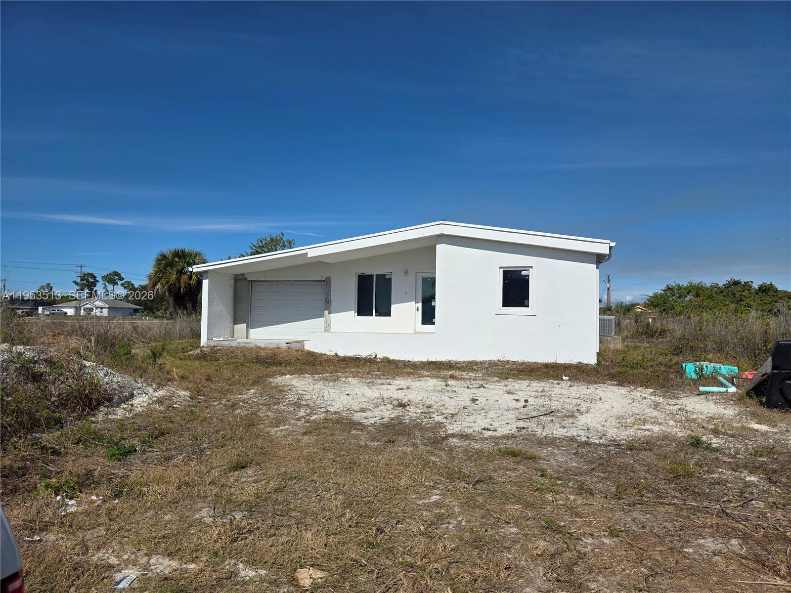 A white, single-story house with a garage and a flat roof sits on a lot — 3030 SW 39TH ST, Lehigh Acres FL 33976, LEHIGH ACRES, FL