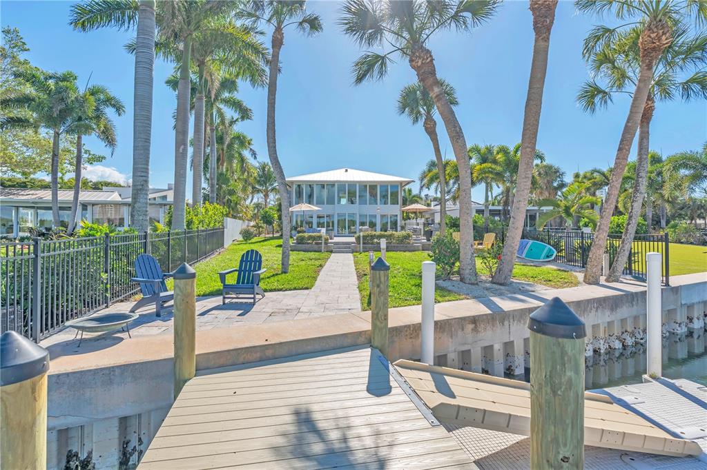 A wooden dock leads to a grassy backyard with a two-story house and palm trees — 701 TYLER DRIVE, SARASOTA, FL