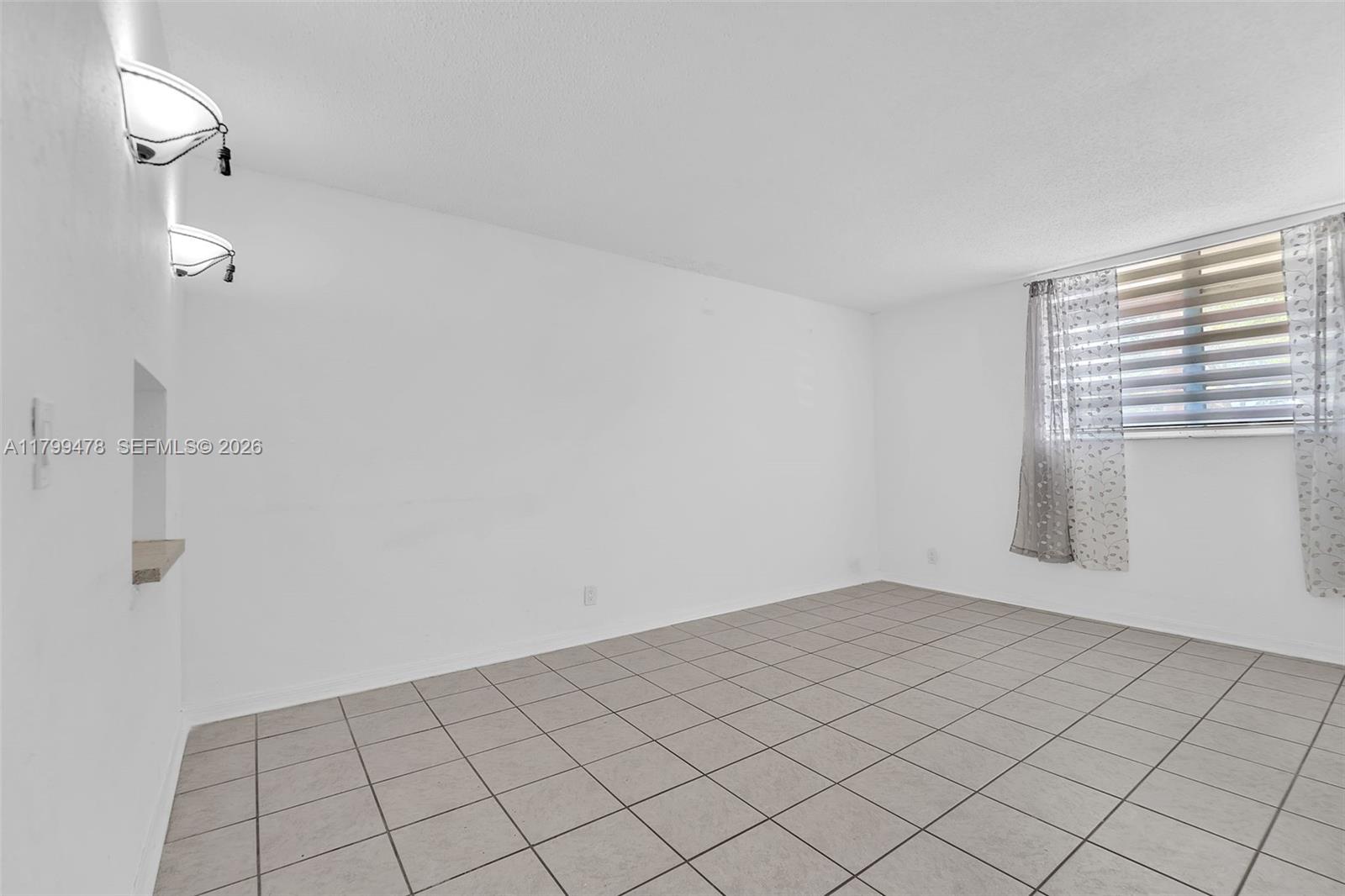 An empty room features white walls, light-colored tile flooring, and a window with blinds — 801 NW 47th Ave # 118W, Miami FL 33126, MIAMI, FL