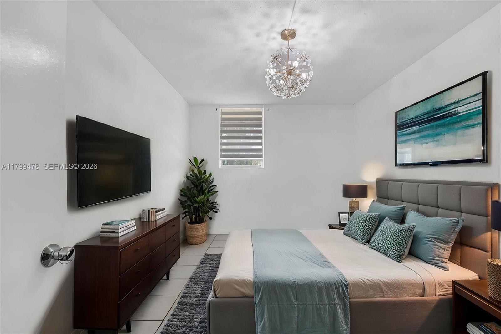 A bedroom features a gray upholstered bed, a dark wood dresser, and a modern chandelier — 801 NW 47th Ave # 118W, Miami FL 33126, MIAMI, FL