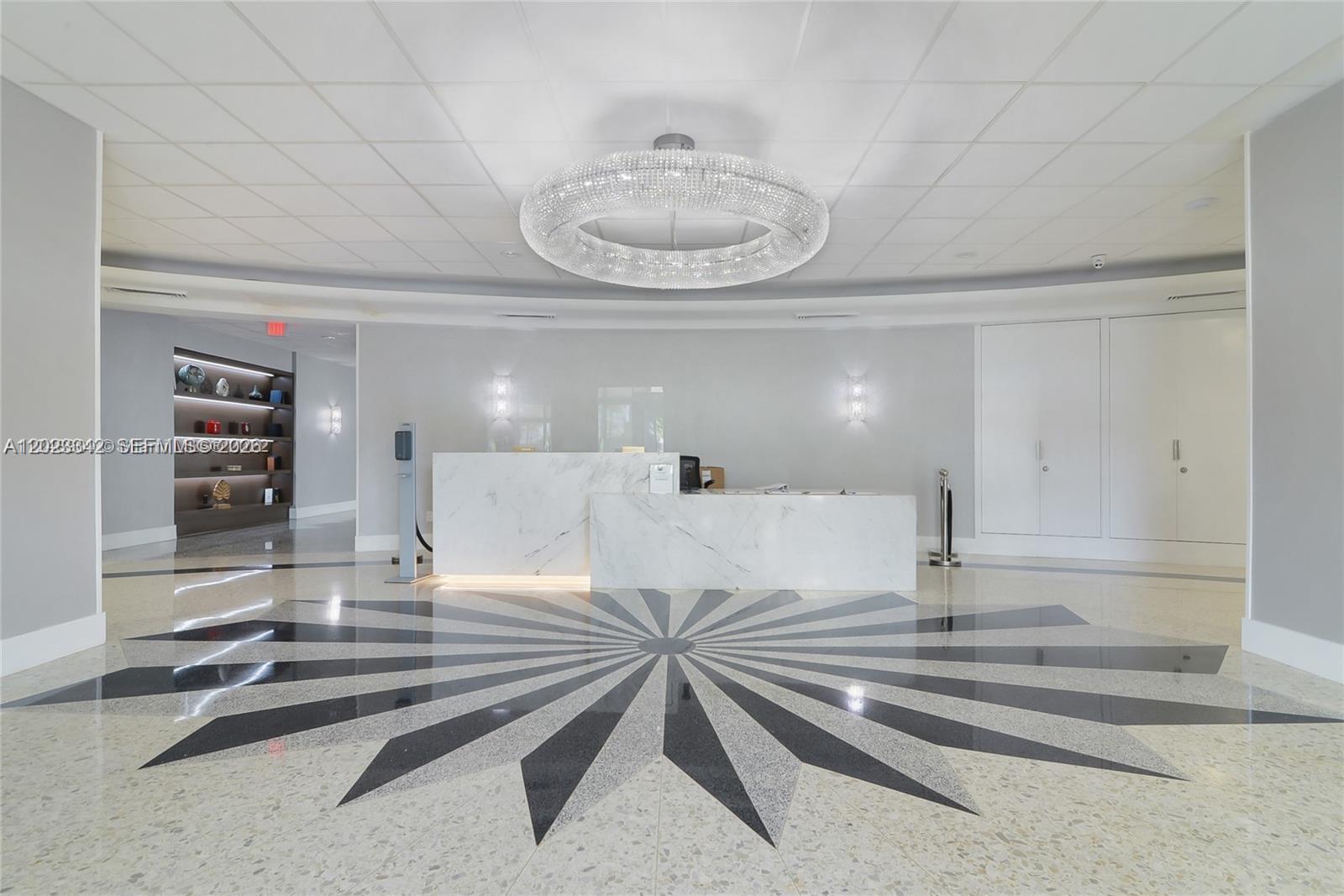 A modern lobby features a marble reception desk, a large crystal chandelier, and patterned flooring — 3140 S Ocean Dr # 1210, Hallandale Beach FL 33009, HALLANDALE BEACH, FL