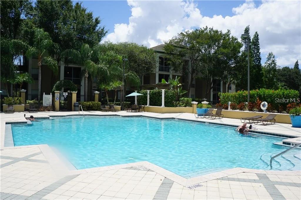 A swimming pool with lounge chairs and palm trees in front of an apartment building — 5817 LEGACY CRESCENT PLACE UNIT 302, RIVERVIEW, FL