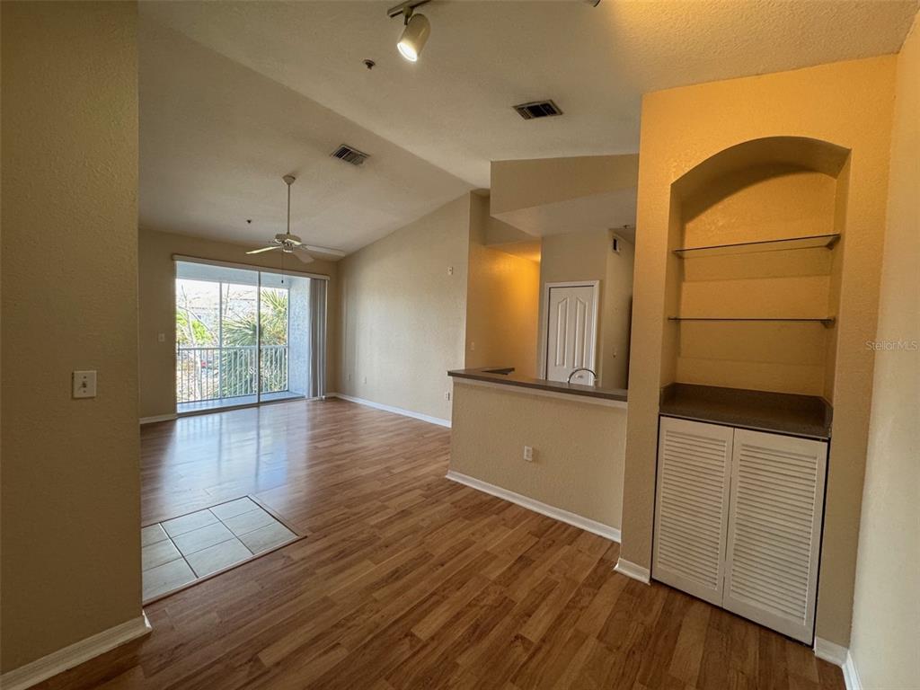 This living area features wood-look flooring, a vaulted ceiling, a balcony, and built-in shelving — 5817 LEGACY CRESCENT PLACE UNIT 302, RIVERVIEW, FL