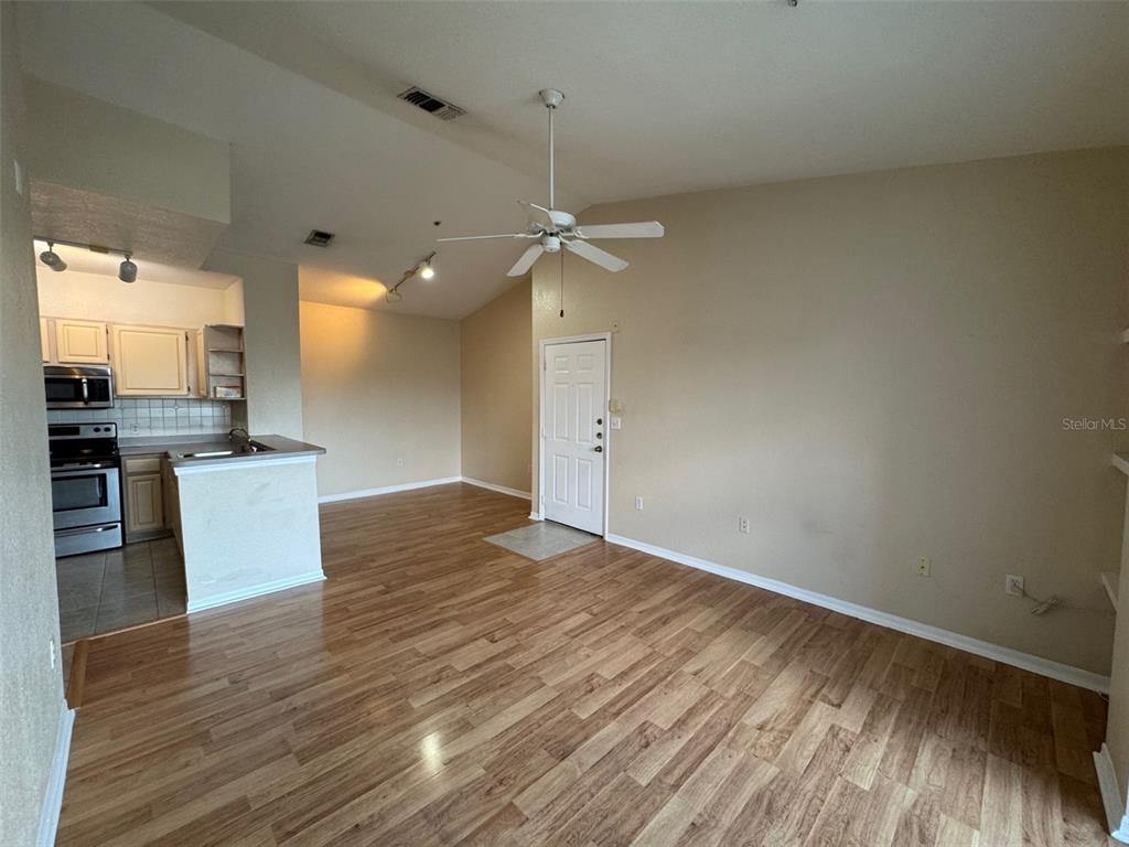 A living room with wood-look flooring and a ceiling fan opens to a small kitchen — 5817 LEGACY CRESCENT PLACE UNIT 302, RIVERVIEW, FL